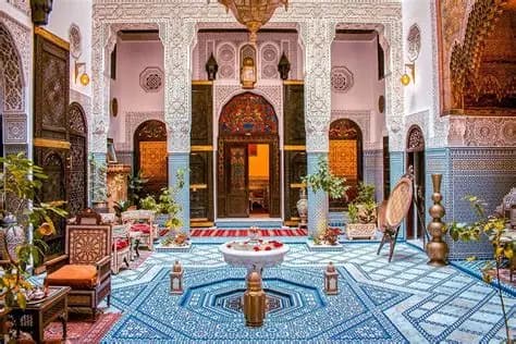 traditional Moroccan riad courtyard with zellige tiles, fountain, carved plaster and greenery